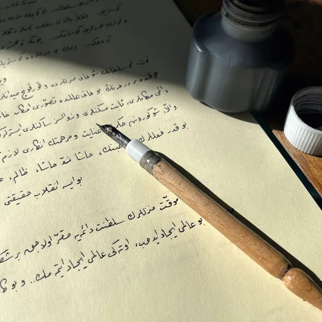 زجاجة حبر وقلم خشبي فوق ورقة بخط عربي