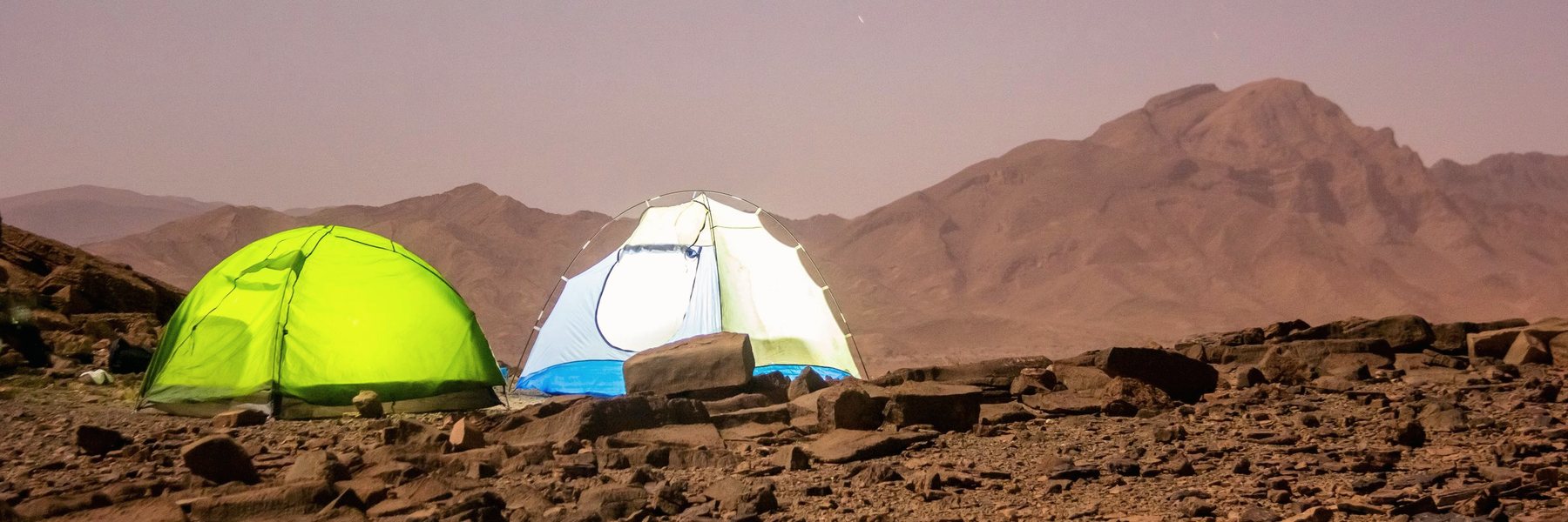 خيمتان منصوبتان على أرض صخرية أمام جبال صحراوية عند الغسق